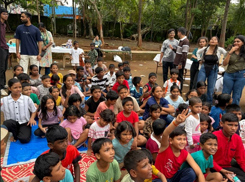 A group of children and volunteers gathered outdoors sitting on mats